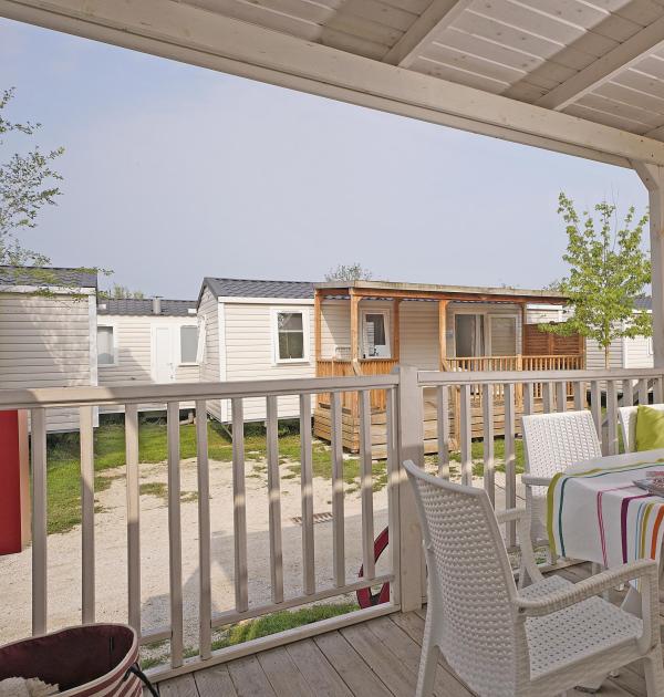 Veranda with table, chairs, and view of mobile homes in a campsite.