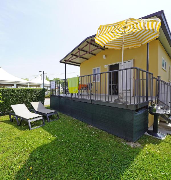 Maison jaune avec terrasse, parasol et chaises longues sur la pelouse.