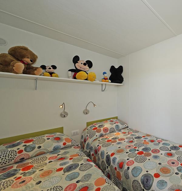 Kamer met eenpersoonsbedden en knuffels op plank.