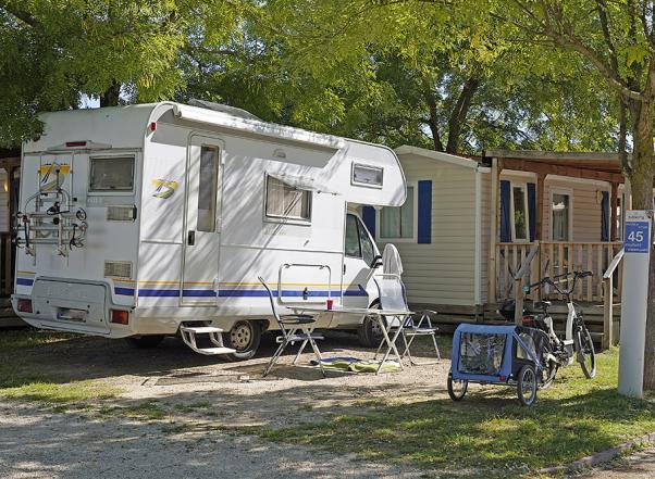 Camper geparkeerd naast een caravan, met fiets en aanhanger.