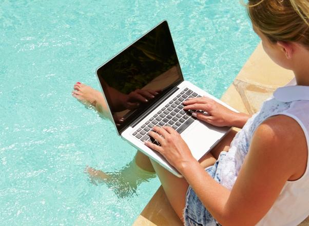 Vrouw werkt op laptop bij het zwembad.