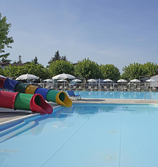 Piscine avec toboggans colorés et transats sous parasols.