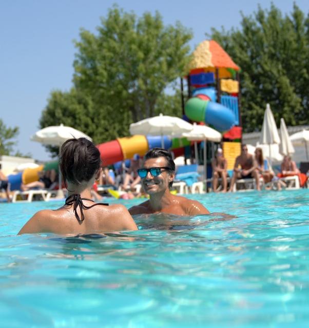 Couple heureux dans une piscine avec des toboggans colorés en arrière-plan.