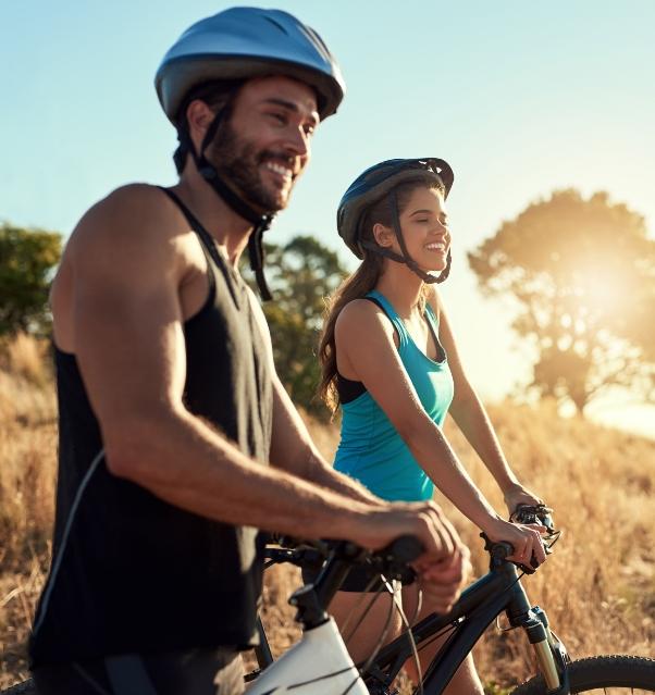 Couple heureux à vélo au coucher du soleil, portant des casques.