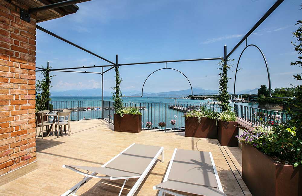 Terras met uitzicht op het meer, ligstoelen, heldere lucht.